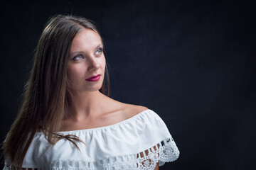 Portrait of a beautiful girl looking up in a loose white dress on a black background