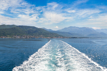 Sea and kielwater seen from ship trail on the water. View of Tivat coastline from ship