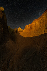 Canyon with a starry sky at night with a moonlit section.