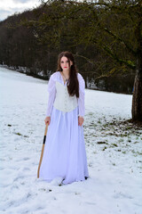 Young girl is standing in long dress in the snow with a bow in hand