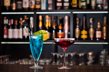 Blue and red cocktails on the bar. Alcoholic cocktails on a background of shelves with bottles. Blurred bottles of alcohol on the wall of the bar.