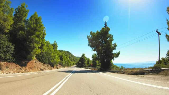 POV drive gopro car travel across beautiful coastal nature, green trees landscape with flickering sunlight, asphalt road point of view