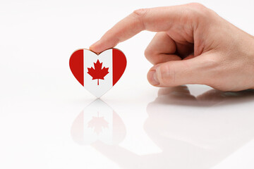 Love and respect Canada. A man's hand holds a heart in the shape of the Canada flag on a white glass surface. The concept of Canadian patriotism and pride.