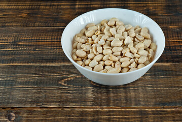 Peanuts in a white bowl on an old shabby board. Nuts on a brown wooden table.