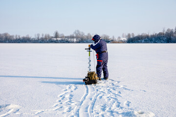 A man drills holes in the ice for ice fishing with an electric auger.