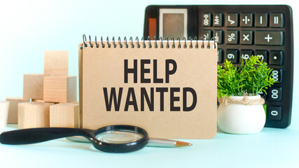 Business concept. Notebook with text HELP WANTED sheet of white paper for notes, calculator, woden blocks, magnifying glass, on the charts background