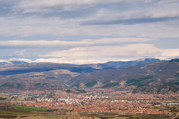 Fototapeta premium View of Pirot city from a vantage point with distant, snow capped mountain peaks in the background and cloudy sky above