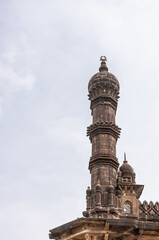 Vijayapura, Karnataka, India - November 8, 2013: Brown stone Nw corner minaret and roof sculptures of Ibrahim Rauza mausoleum under light blue cloudscape. 