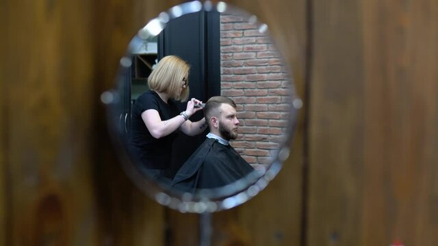 Woman barber cuts the client. View in a round table mirror