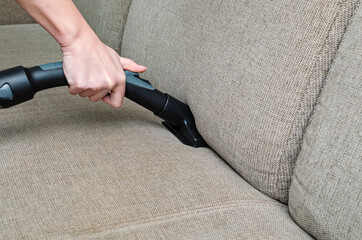 woman vacuums the gray sofa with a washing vacuum cleaner. Cleaning and cleanliness concept - obrazy, fototapety, plakaty