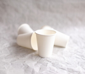 disposable cups made of white paper are laid out on gray crumpled paper