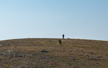 Obraz premium Silhouette of a young man running to the top of a high hill on a clear sunny day.