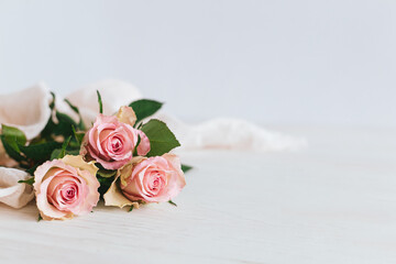 Tender pink roses on white wooden background. Greeting card for Women's day.