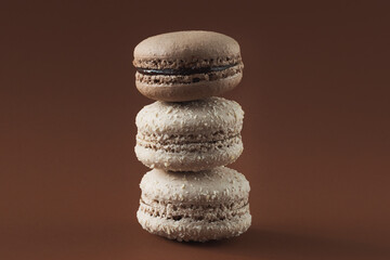 Chocolate macaroons in coconut flakes lay on top of each other. Brown background, horizontal photo. Delicious French pastries.