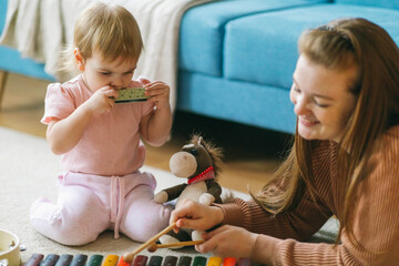 Mother and one and a half year old girl play musical instruments: xylophone, harmonica, tambourine. Early musical education of children