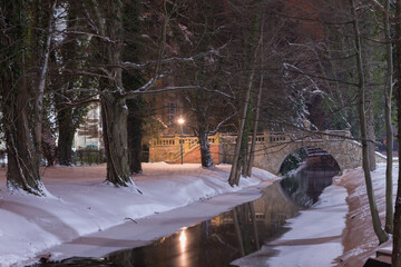 Park Dworski w Iłowej w zimową noc. Kamienny mostek nad rzeką.