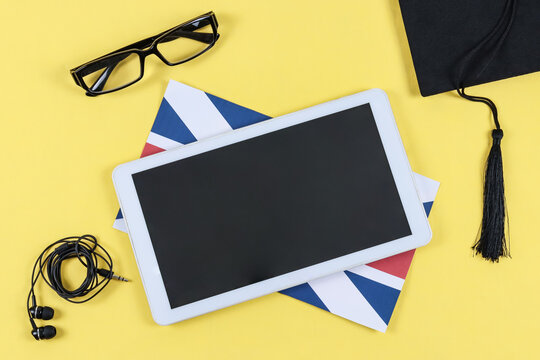 back to school.
Tablet and academic cap with glasses, headphones and the British flag on a yellow background with a place for text, top view close-up.