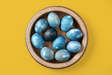 Aquamarine easter eggs in ceramic bowl on yellow background