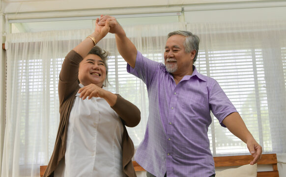 Spending Time Together At Home, An Elderly Asian Couple Having Fun Dancing In The Living Room.