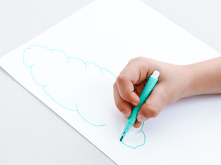 hand with pen.
Children's hand with a pen draws a cloud on a white sheet of paper, close-up side view.