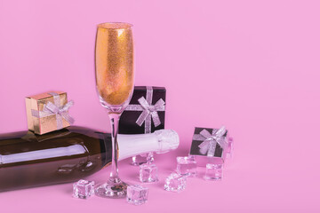 Creative minimal concept made of champagne bottle and  glass of golden glitters, ice cubes and gift box on pastel pink background