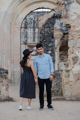 Fototapeta na wymiar Young couple on vacation visiting famous Santiago Cathedral ruins in Antigua Guatemala - Travelers enjoying their romantic vacations - Couple holding hands looking at each other