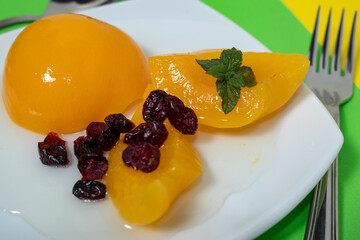 delicious peaches in syrup in a glass bowl on a colored surface and some cranberries.