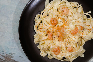 Delicious Italian pasta. Fetuccini with shrimp and herb sauce on black plate and light background.