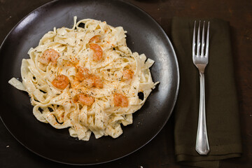 Delicious Italian pasta. Fetuccini with shrimp and herb sauce on black plate and dark background.