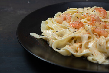 Delicious Italian pasta. Fetuccini with shrimp and herb sauce on black plate and dark background.