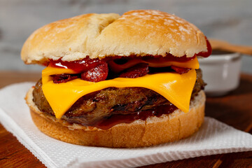 Delicious hamburger with Bacon and cheddar cheese on homemade bread with seeds and ketchup on a wooden surface and rustic background.