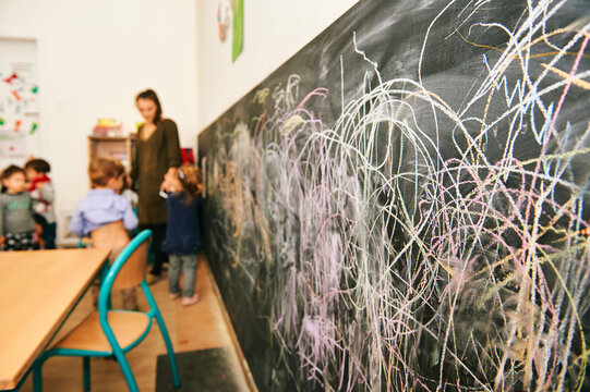 Art classroom in kindergarten, young teacher drawing with children on chalk wall