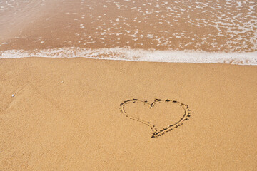 Heart painted on the sand on the beach and foam from the waves.