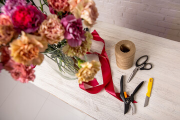 Florist's workplace. Tools and flowers before starting work on the table. Floristic's knife, scissors, pruning shear, tape, twine. Top view. Tutorial. Step by step
