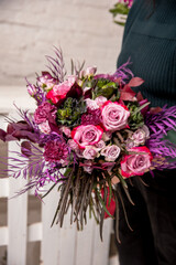 Florist's workplace in a loft space. An experienced florist composes a bouquet of roses, carnations and eucalyptus, adding flowers step by step. She examines the assembled bouquet. Tutorial