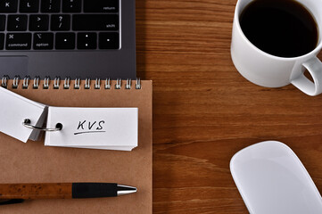 On the desk there is a laptop, a cup of coffee, and a word book with the word KVS written on it. It was an abbreviation for the financial term key value store.