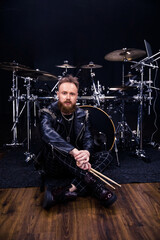 Fototapeta premium brutal portrait of a man musician with a beard and in black clothes on the background of musical instruments drums