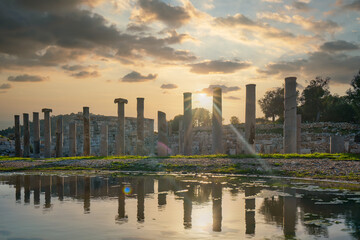 Patara ancient city columns with reflection on water. Cloudy sunset at Patara