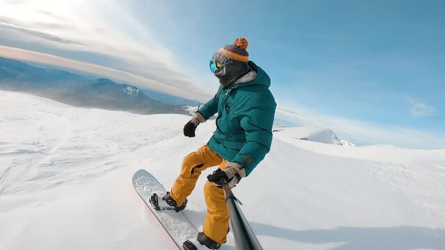 Guy filming himself during riding down. Man riding on snowboard with selfie stick in his hand downhill kamchatka mountain. Concept of extreme, sport, winter, freeride, snowboarding