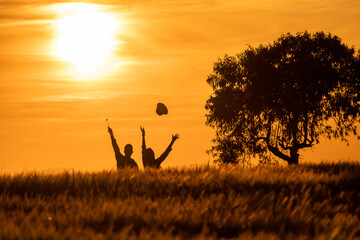 silhouette of girl and boy throwing hats in the air at sunset in the countryside