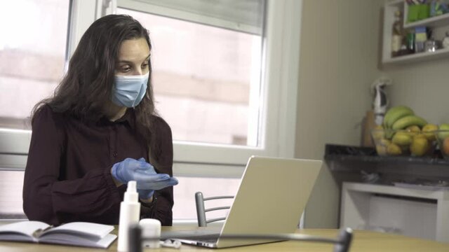 Young enterprising girl with burgundy shirt, mask and latex gloves, making a video call from home moving her hands on wooden table. black hair business woman telecommuting. student giving virtual clas