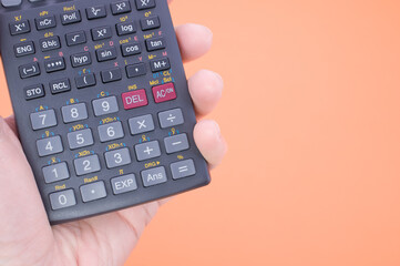 A scientific calculator on a person's hand against an orange background with space for your text