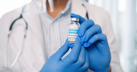 Close up shot of healthcare worker specialist in protective uniform holding in hands in gloves ampoule with coronavirus vaccine, covid-19 vaccination concept, virus cure medicament, healthcare