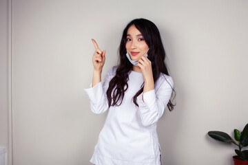 young asian woman doctor in white uniform gesturing positive on gray background, wearing a mask, lifestyle healthcare people concept