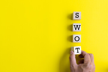 hand putting wooden cube with swot analysis on yellow background and copy space. strategy idea concept.