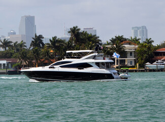 Fototapeta na wymiar Black and white motor yacht cruising by RivaAlto Island with Miami tall building skyline in the distant background.