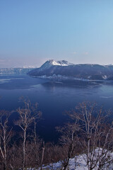 雪に覆われた山と冬の或る山間の湖の明媚。日本の北海道の阿寒摩周国立公園の摩周湖。