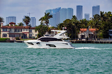 Luxury white motor yacht cruising by RivaAlto island in Miami Beach,Florida with Miami tall building skyline in the background ..