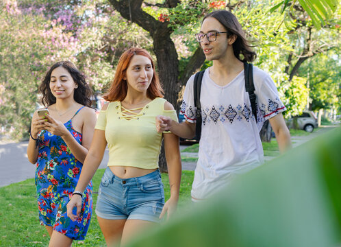 group of friends walking in the neighborhood.  Young people walking around the green park.