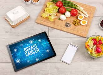 BREAST CANCER concept in tablet pc with healthy food around, top view